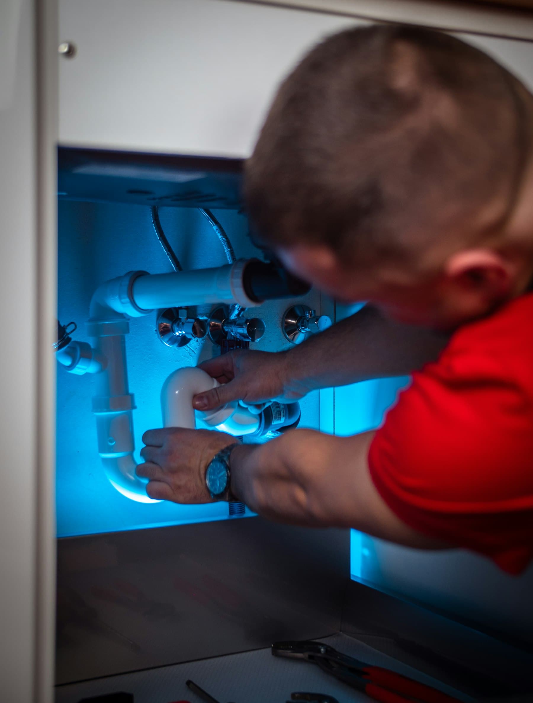 A technician working on plumbing under a cabinet